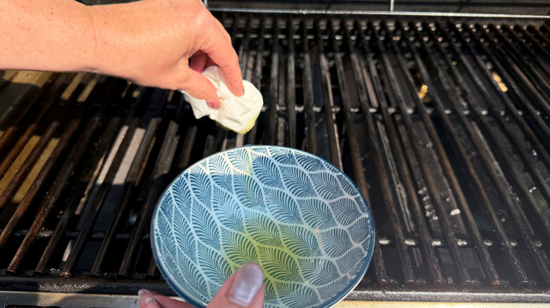 Hand using paper towel to brush oil onto grill grates
