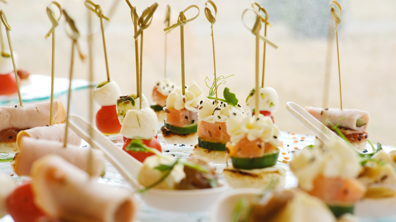 A plate of fancy wedding hors d'oeuvres served on toothpicks.
