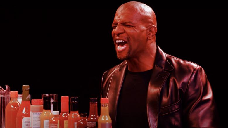 Terry Crews wincing on Hot Ones in front of hot sauce lineup