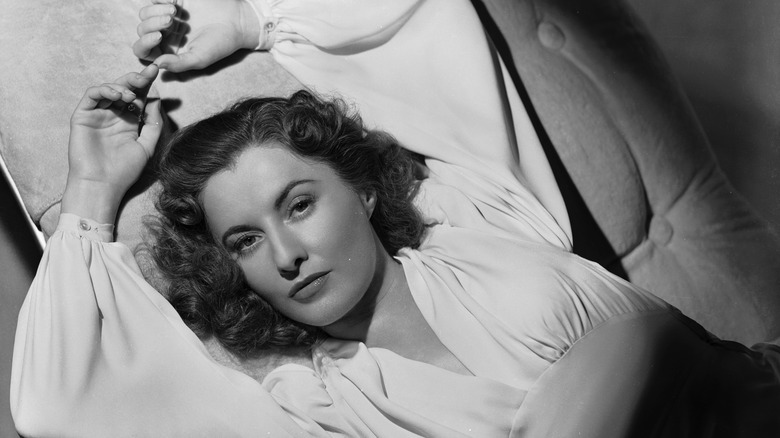 Actor Barbara Stanwyck lounging an a chaise with her arms overhead.
