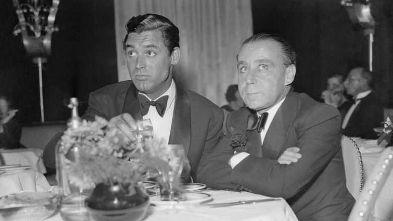 Actor Cary Grant and producer A.C. Blumemthal, dressed in black tie, seated at restaurant.
