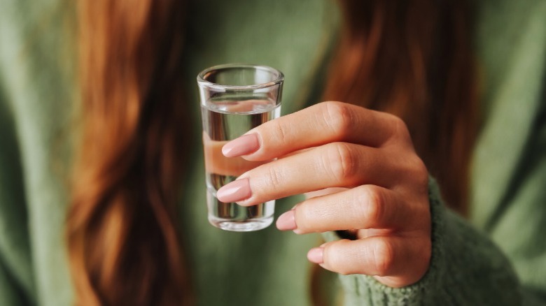 Manicured hand holding shot glass of vodka.