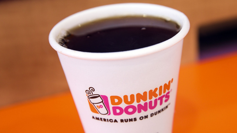  leaning cup of Dunkin' coffee