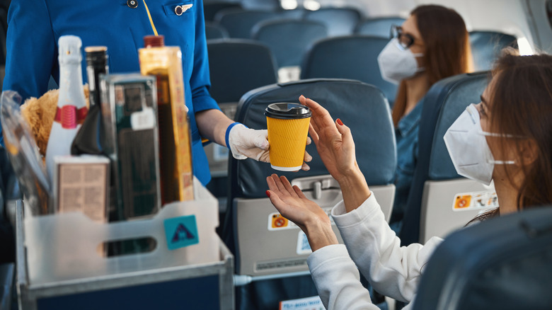 A flight attendant handing over coffee to a traveler