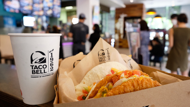 Taco Bell cup and tacos with restaurant interior in background.