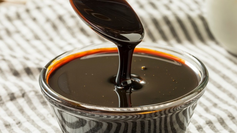 A spoon hovering above a glass of dark molasses