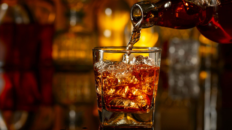 Pouring whiskey into a tumbler with ice