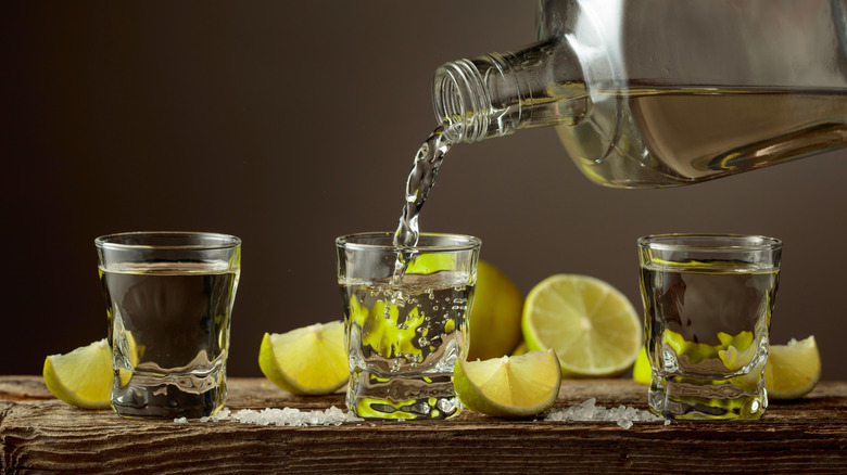 Blanco tequila poured into a shot glass with lemon wedges in the background