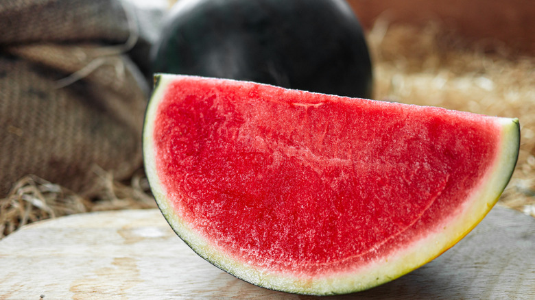 A bright red watermelon quarter sits on the ground.
