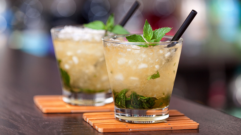 Two mint julep cocktails with black straws on wooden bar.