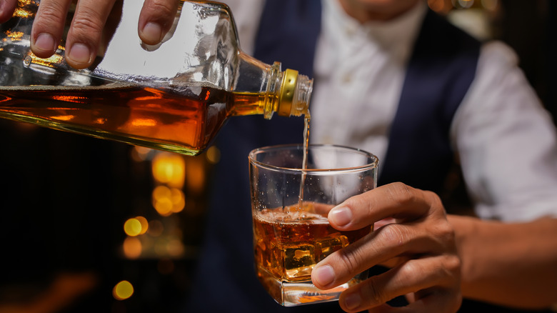 Bartender pouring bourbon from bottle into glass.