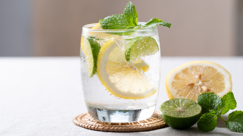 Clear sparkling beverage in glass with lemon & lime slices and garnish on coaster atop white table