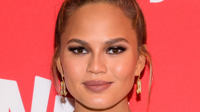 A close up of Chrissy Teigen wearing a high bun and gold earrings