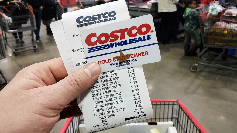 Hand holding Costco membership card and receipt in busy store