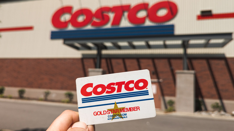 Costco gold star member card held in front of Costco building