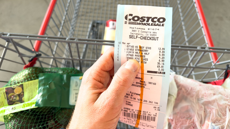 Hand holds a Costco receipt in front of a shopping cart