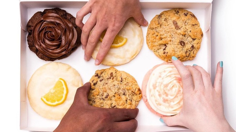 Hands reaching for Crumbl Cookies