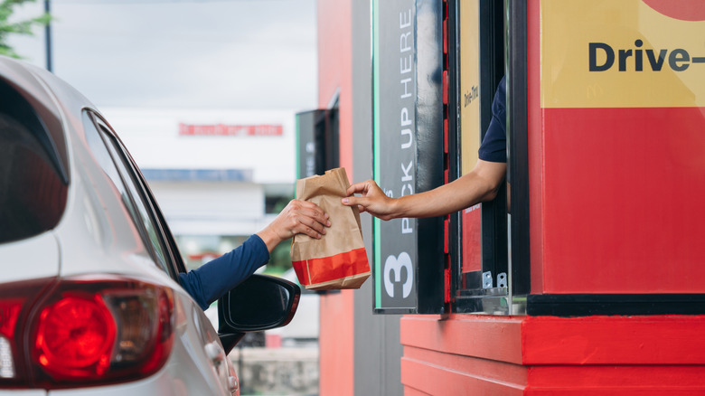 Person in car receives a paper bag of food from a drive-thru restaurant