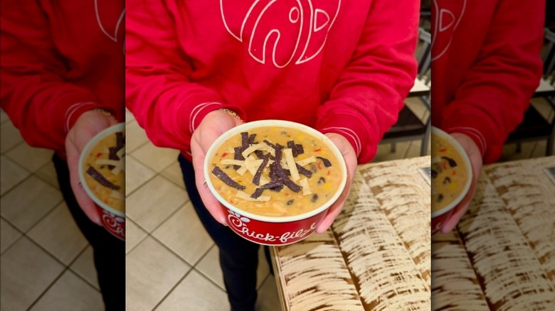 Chick-fil-A employee in red shirt with nametag holding paper bowl of chicken tortilla soup