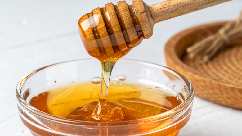 Honey dripping off dipper into small glass bowl.