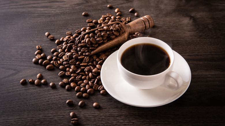 Cup of black coffee and coffee beans on table