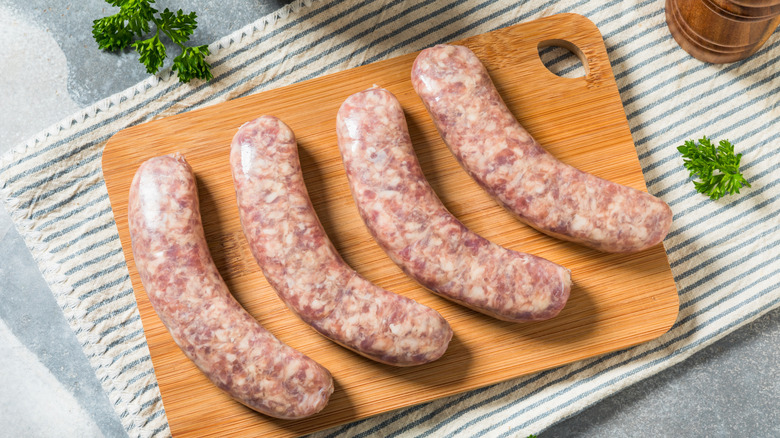 Fresh links of raw bratwurst set next to each other with salt and herbs surrounding.