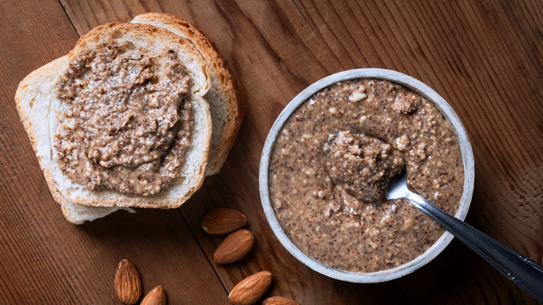 Almond butter spread on toast next to a jar of almond butter set on a wooden table