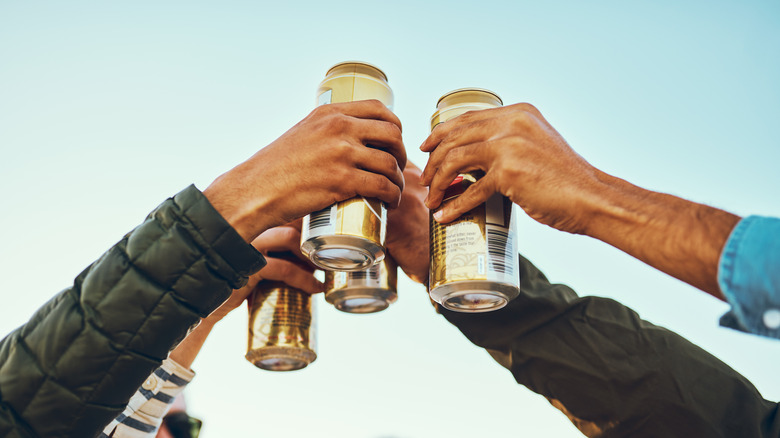 Four people toasting beer cans