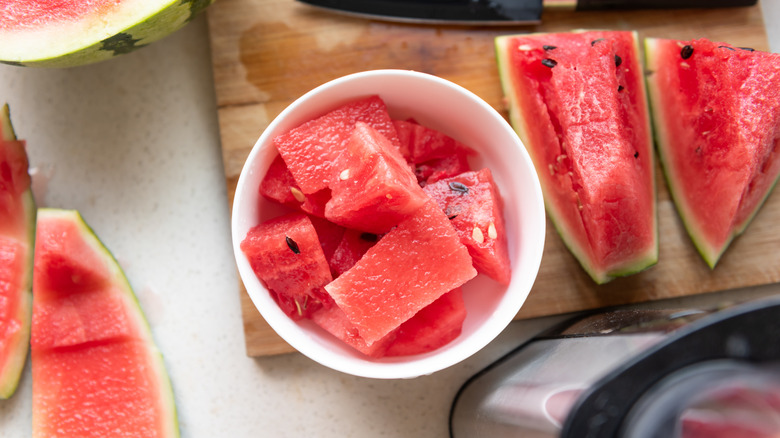 Cut watermelon in a bowl and a carving board where a knife rests.