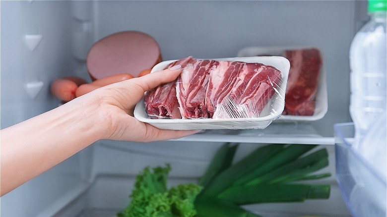 person taking container of raw beef out of the fridge