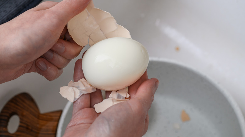 A hand peeling a hard-boiled egg over the sink into a bowl