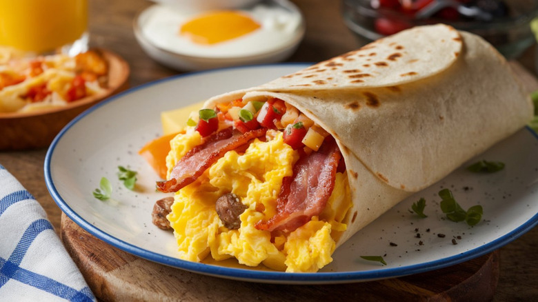 Breakfast burrito with scrambled eggs, bacon, and other accoutrements, wrapped in a flour tortilla.