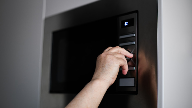Hand setting dial on wall-mounted microwave.