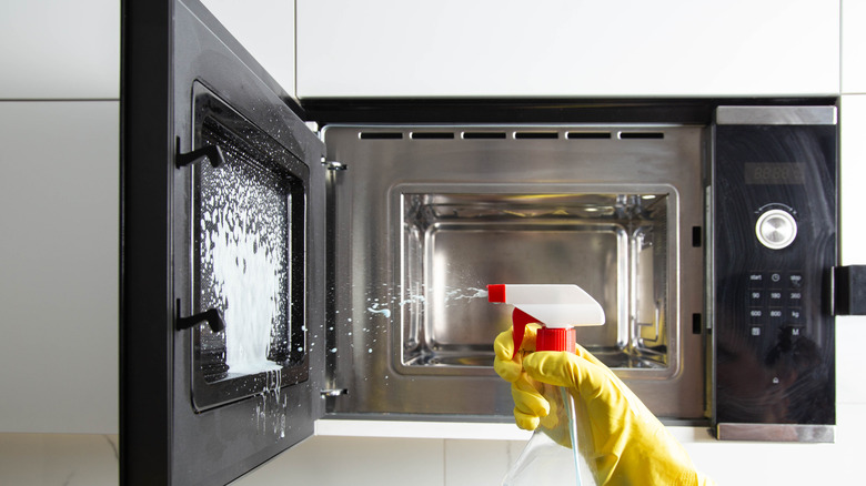 Person spraying cleaner on microwave interior.