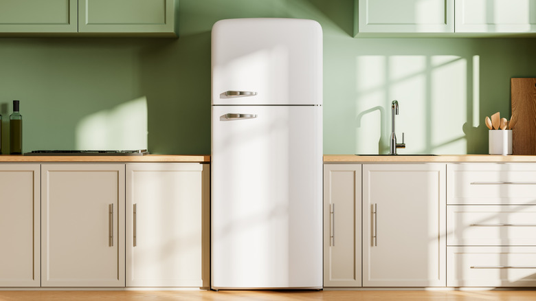 White refrigerator in kitchen with green wall and cabinets