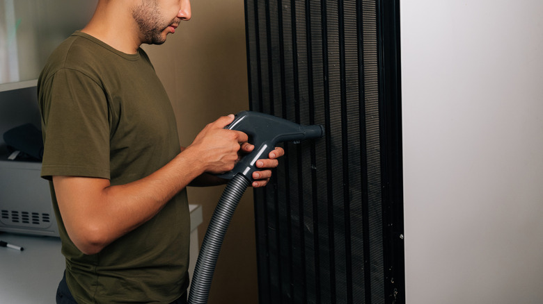 Person vacuums condenser coils on a refrigerator