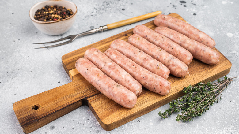 Sausage links on cutting board over stone surface, peppercorns, grill fork, and sprig of thyme