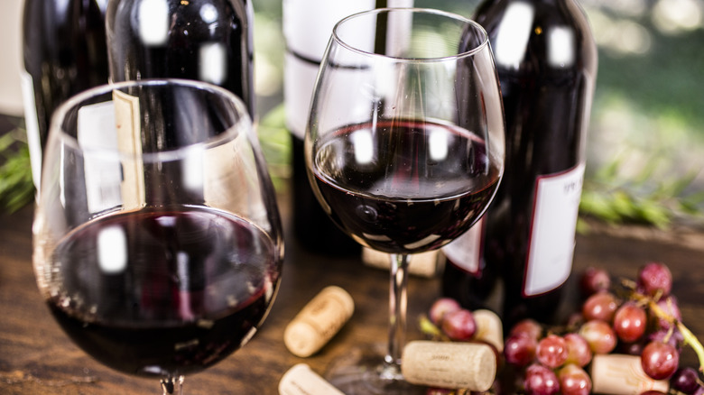 Glasses of red wine with bottles, corks, and grapes