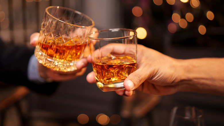 Two people clinking glasses of bourbon