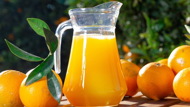 Pitcher of orange juice surrounded by oranges.