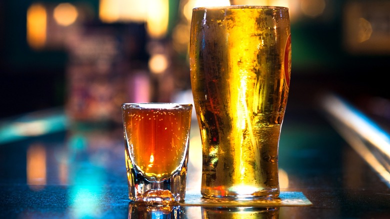 A pint of beer next to a shot of whiskey at a bar.