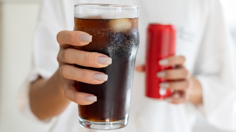 Person holding a glass of cola with a red can in the background