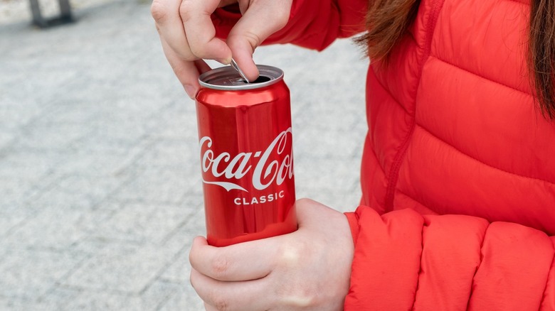 Person opening a can of Coca-Cola classic