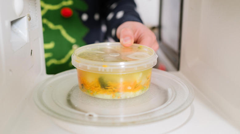 Hand placing plastic container of soup in microwave.