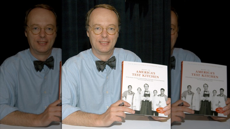 Christopher Kimball smiling while holding an "America's Test Kitchen" cookbook