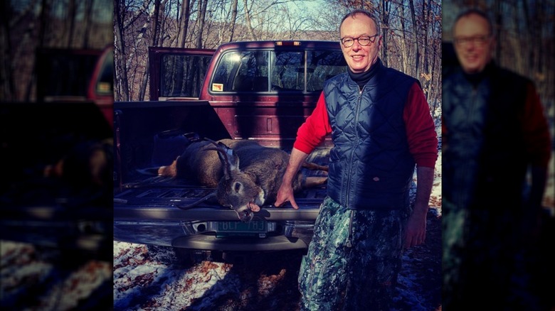 Christopher Kimball posing with a deer he hunted that's in the back of a truck
