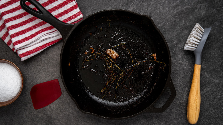 dirty cast iron skillet being prepared for cleaning next to a bristle brush and cloth