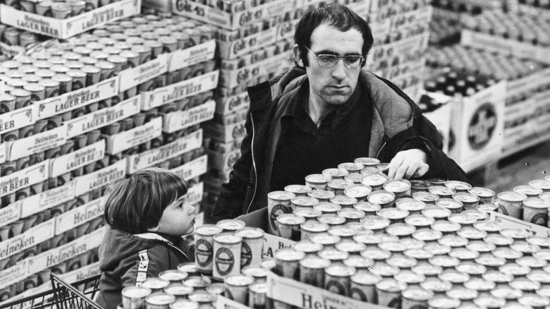 Man shopping for beer with small child in shopping cart, 1970s.