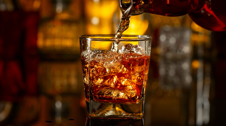 Bottle pouring whiskey into a glass with ice.