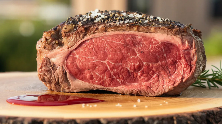 Cross-section cut of cooked prime rib with salt and pepper crust on cutting board